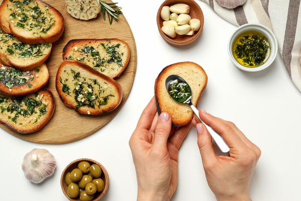 Garlic bread, hands, bowls with oil, olives and garlic on white